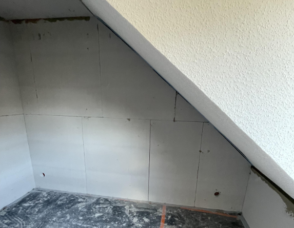 Schräge Decke über heller Plattenverkleidung, Boden mit grauen Staubresten.