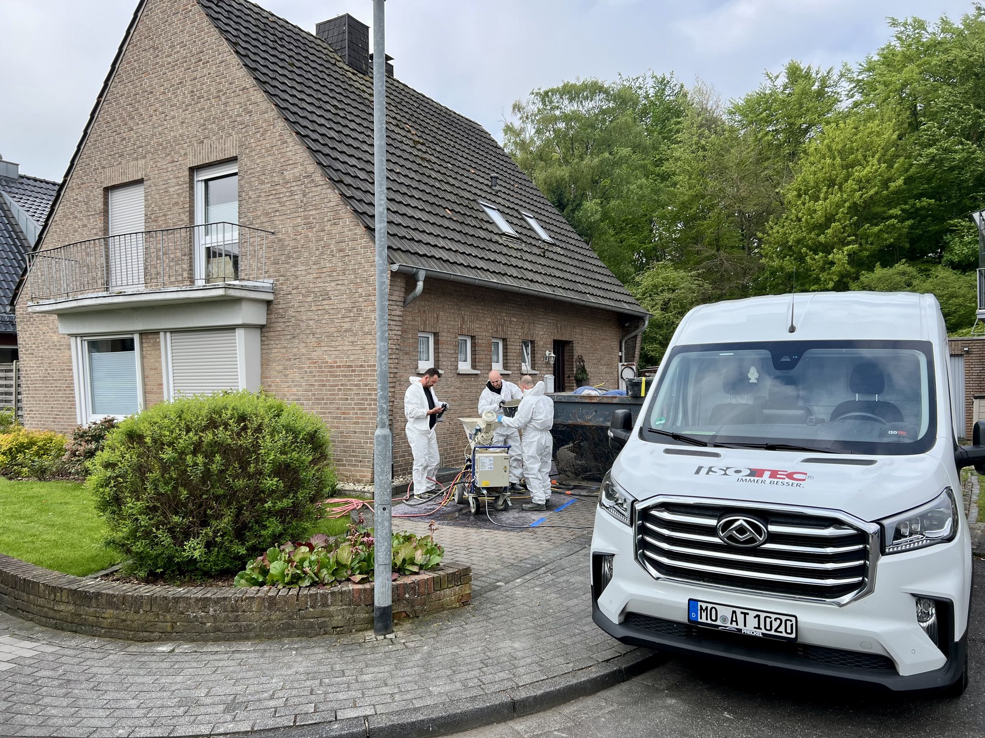 ISOTEC Mitarbeiter arbeiten mit Maschine vor Wohnhaus in Einfahrt.