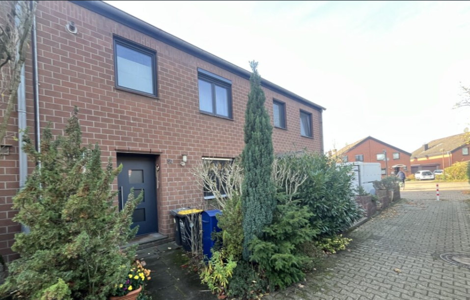 Reihenhaus mit Klinkerfassade, Eingang und Sträuchern an gepflasterter Zufahrt