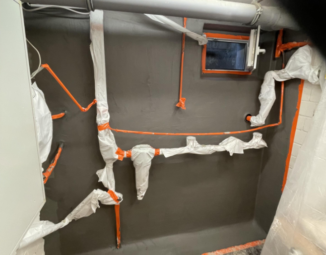 Abgeklebte Rohre vor dunkel beschichteter Kellerwand mit kleinem Fenster