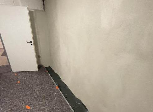 Helle verputzte Wand mit schwarzer Folie am Bodenrand in einem Raum