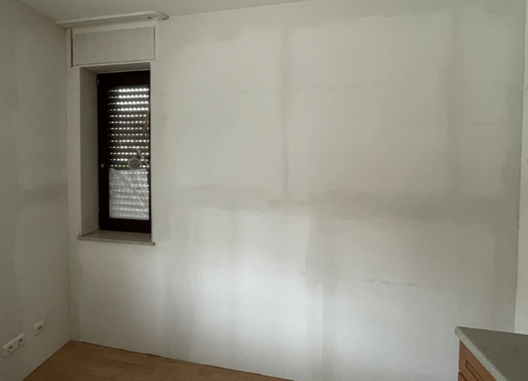 Weiß gestrichene Zimmerwand mit ausgebesserten Flächen neben Fenster
