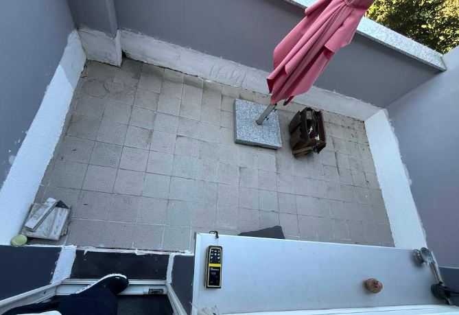 Gelbes Feuchtigkeitsmessgerät liegt auf weißer Kante einer Terrasse mit beigen Bodenfliesen.
