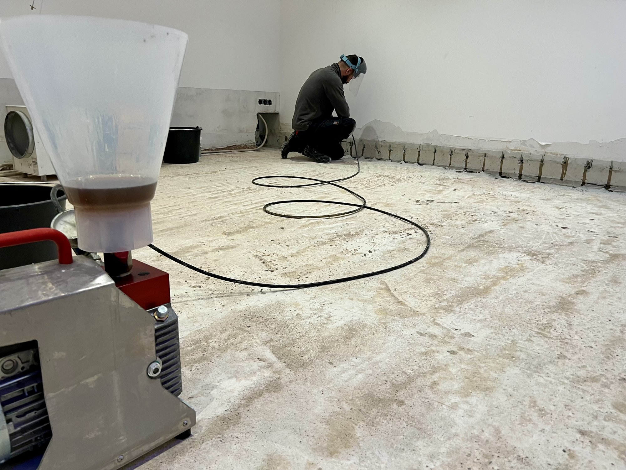 Arbeiter bohrt Löcher entlang der Wand über freigelegtem Betonboden.