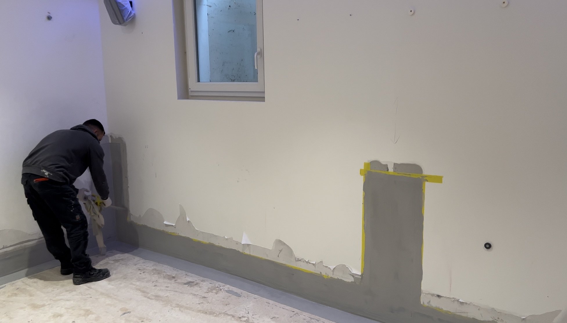 Arbeiter trägt graue Masse auf Wand im Raum auf.