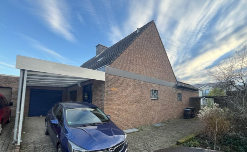 Backsteinhaus mit Carport und gepflasterter Einfahrt unter wolkigem Himmel