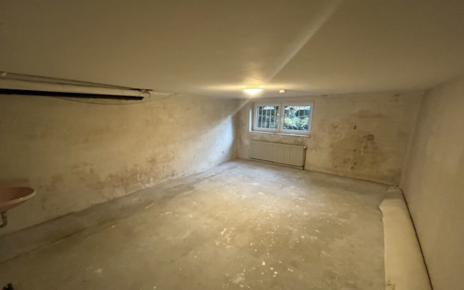 Leerer Kellerraum mit fleckigen, beschädigten Wänden und kleinem Fenster