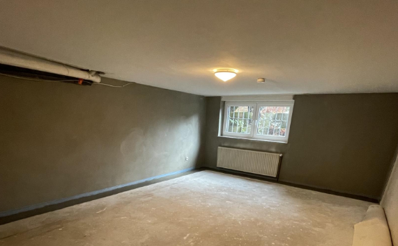 Leerer Kellerraum mit grauen Wänden, Fenster und Heizkörper