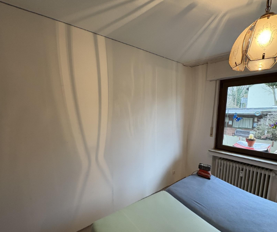 Leeres Zimmer mit Bett, weißer Wand und Fenster neben Heizkörper