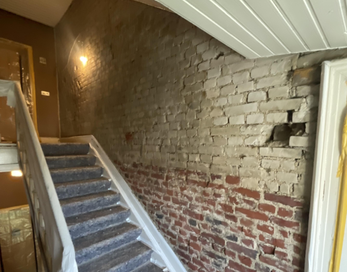 Treppenhaus mit freigelegter Ziegelwand und Putzresten, seitliche Perspektive