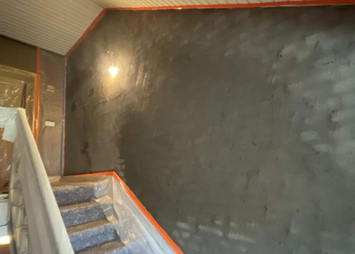 Abgeklebtes Treppenhaus mit dunkelgrau beschichteter Wand und abgedeckten Stufen