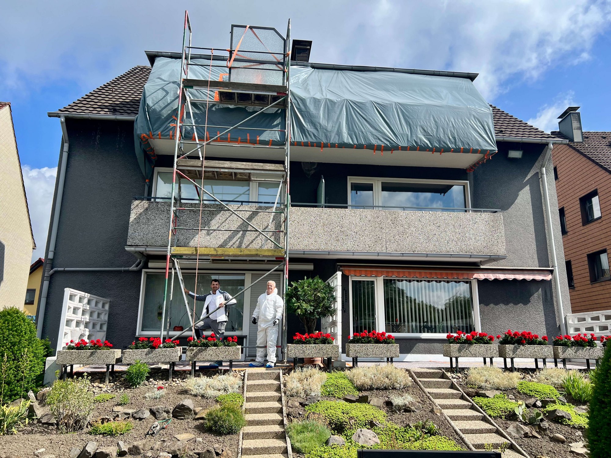 Geruest an Hausfassade, Balkon mit Folie abgedeckt, zwei Arbeiter davor
