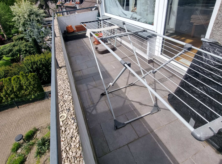 Wäscheständer auf gefliestem Balkon neben Glasschiebetür, Blick nach unten.