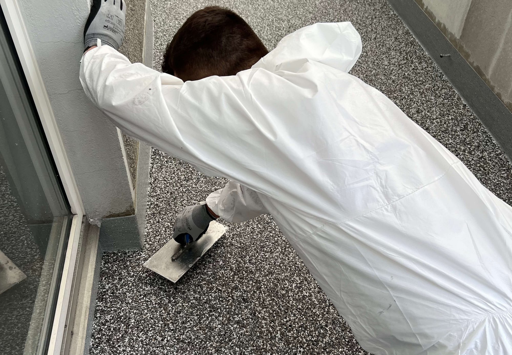Arbeiter trägt schwarze Masse mit Kelle an Sockel neben Schiebetuer auf.