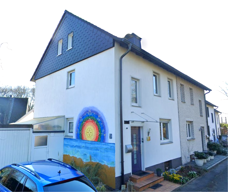 Wohnhausfassade mit buntem Wandgemälde, Eingangstür und geparktem blauem Auto.