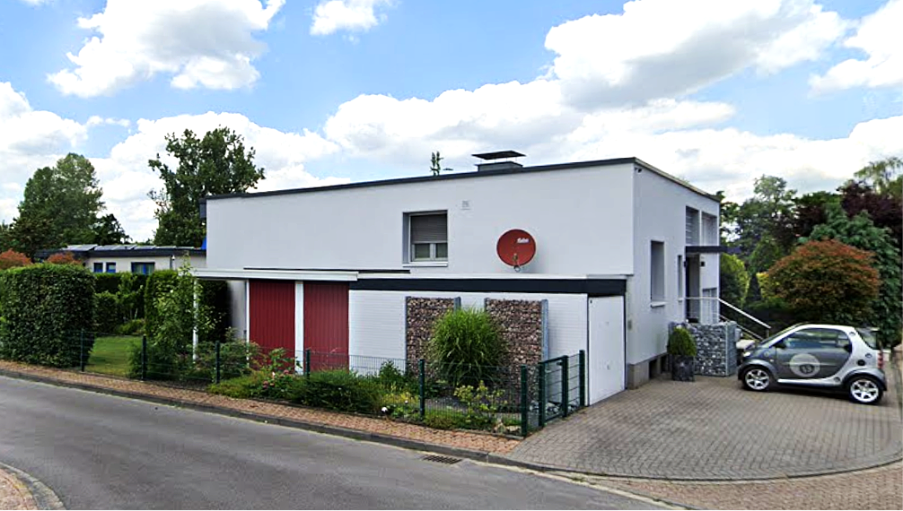 Modernes Flachdachhaus mit Einfahrt, Hecke und parkendem Kleinwagen an der Straße