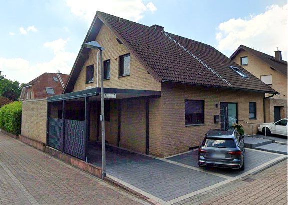 Gelbes Ziegelhaus mit braunem Dach und Carport in Wohnstraße, davor parkt dunkler Kombi.