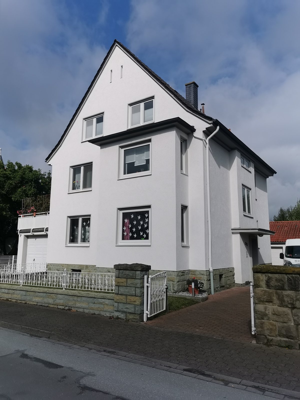 Weißes Wohnhaus mit Satteldach und Vorgartenzaun vor strahlend blauem Himmel
