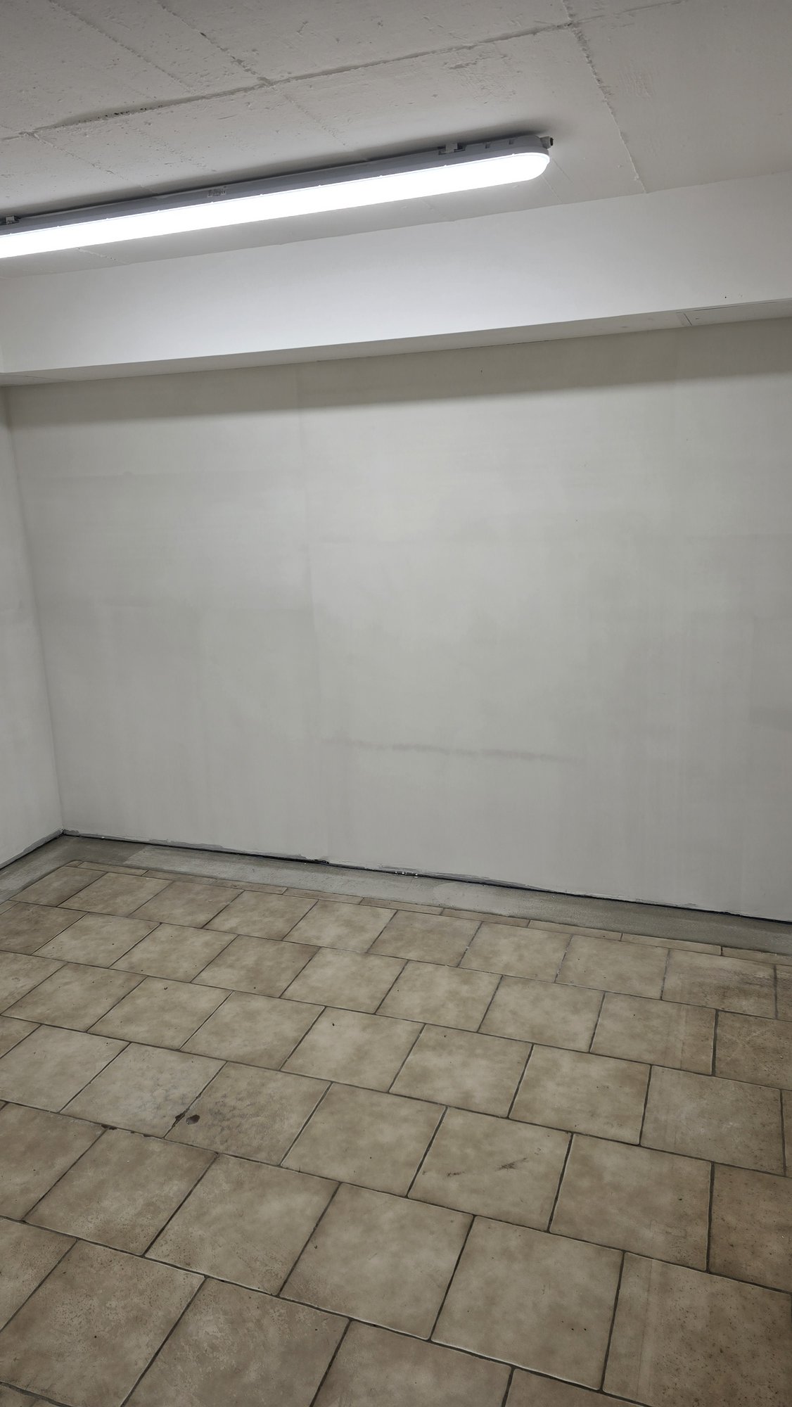 Weiße Kellerwand mit hellen Ausbesserungen über Fliesenboden