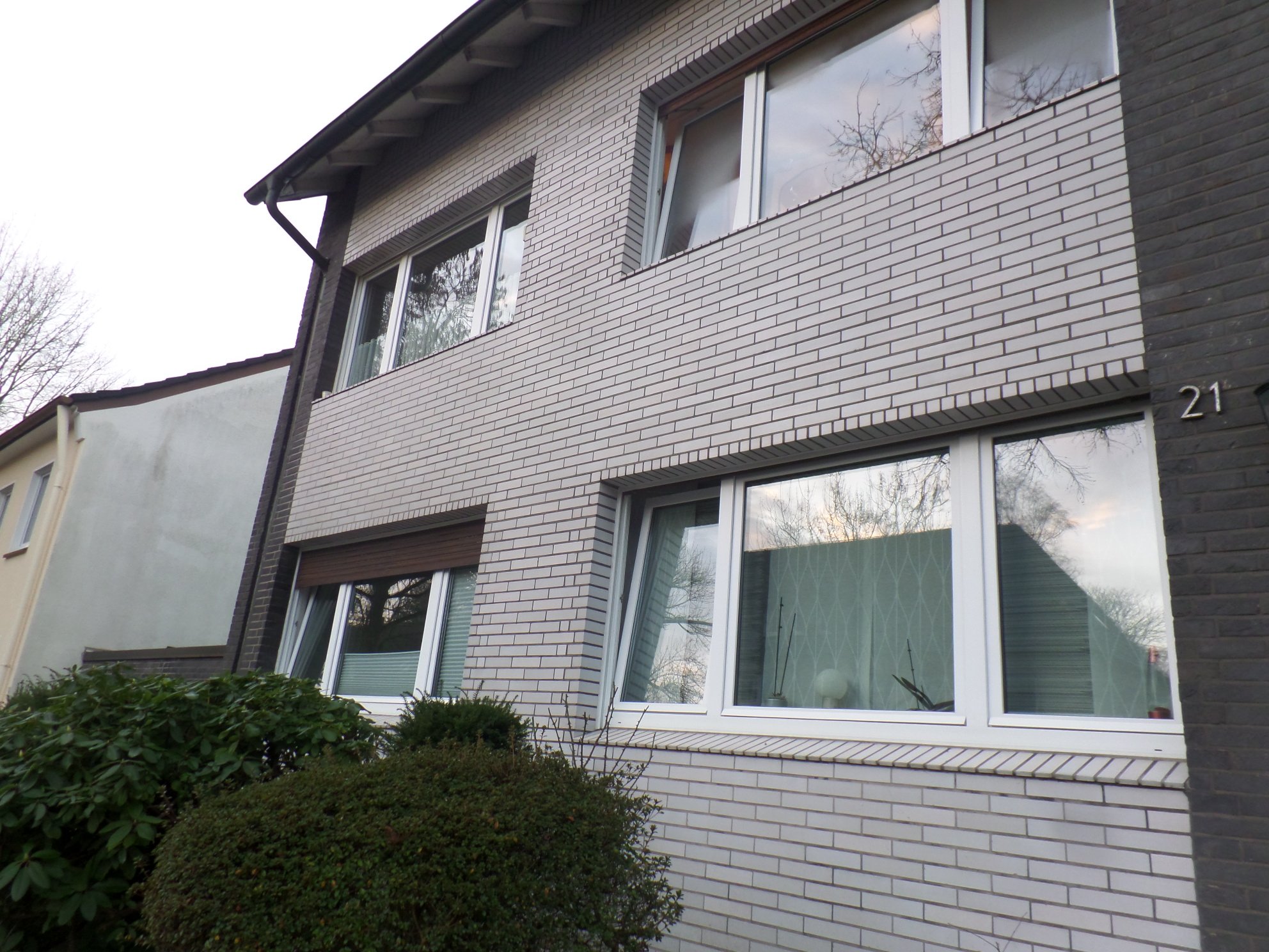 Fassade mit hellen Klinkern, weißen Fensterrahmen und Hausnummer 21.