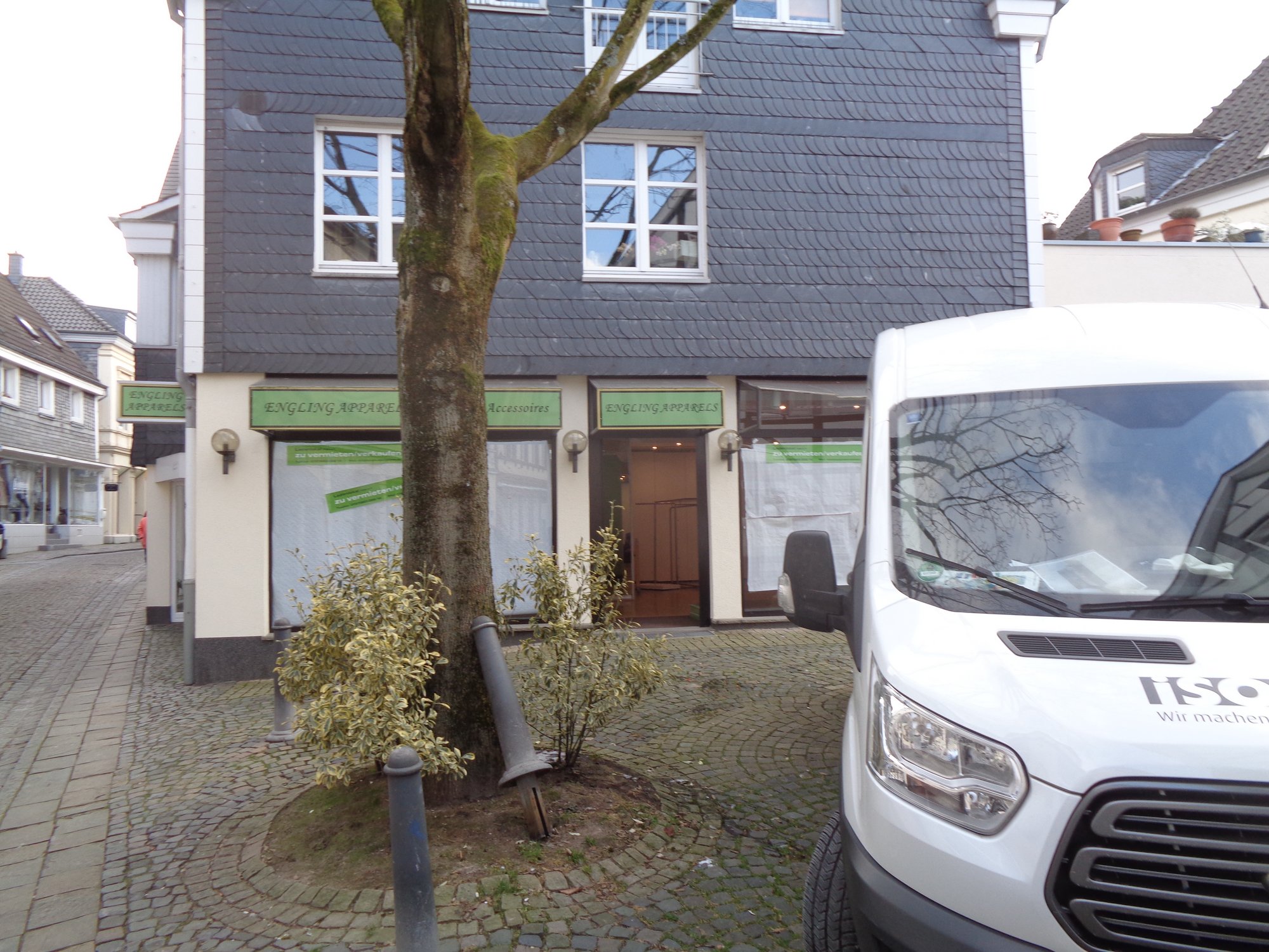 Schieferfassade mit Schaufenstern und Baum am Gehweg, Transporter vorne rechts