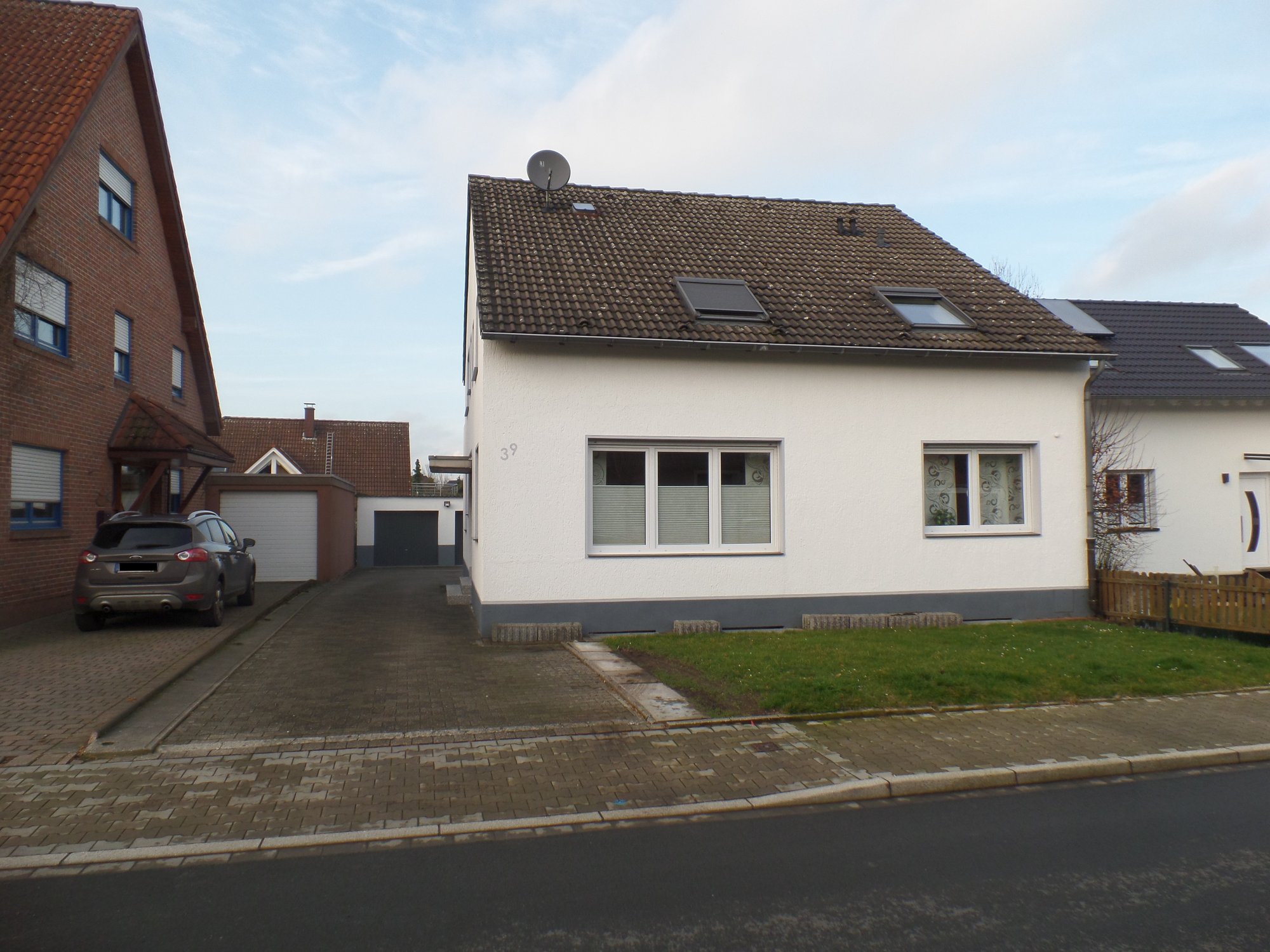 Einfamilienhaus mit weißer Fassade, Ziegeldach und Vorgarten an einer Straße