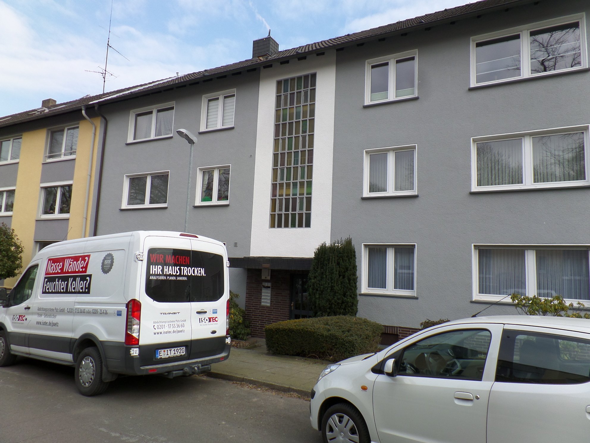 ISOTEC Transporter vor Wohnhaus mit grauer Fassade und Glasbaustein-Treppenhaus