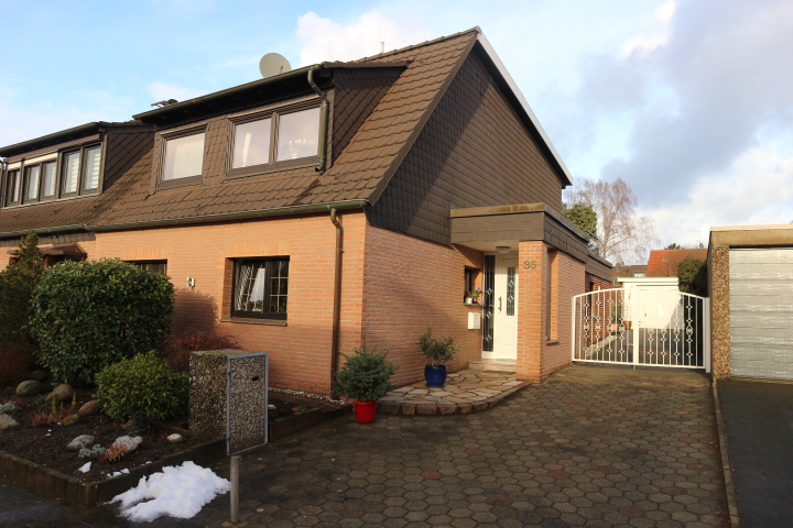 Einfamilienhaus mit Klinkerfassade, gepflasterter Einfahrt, Gartenecke und Schneeresten.