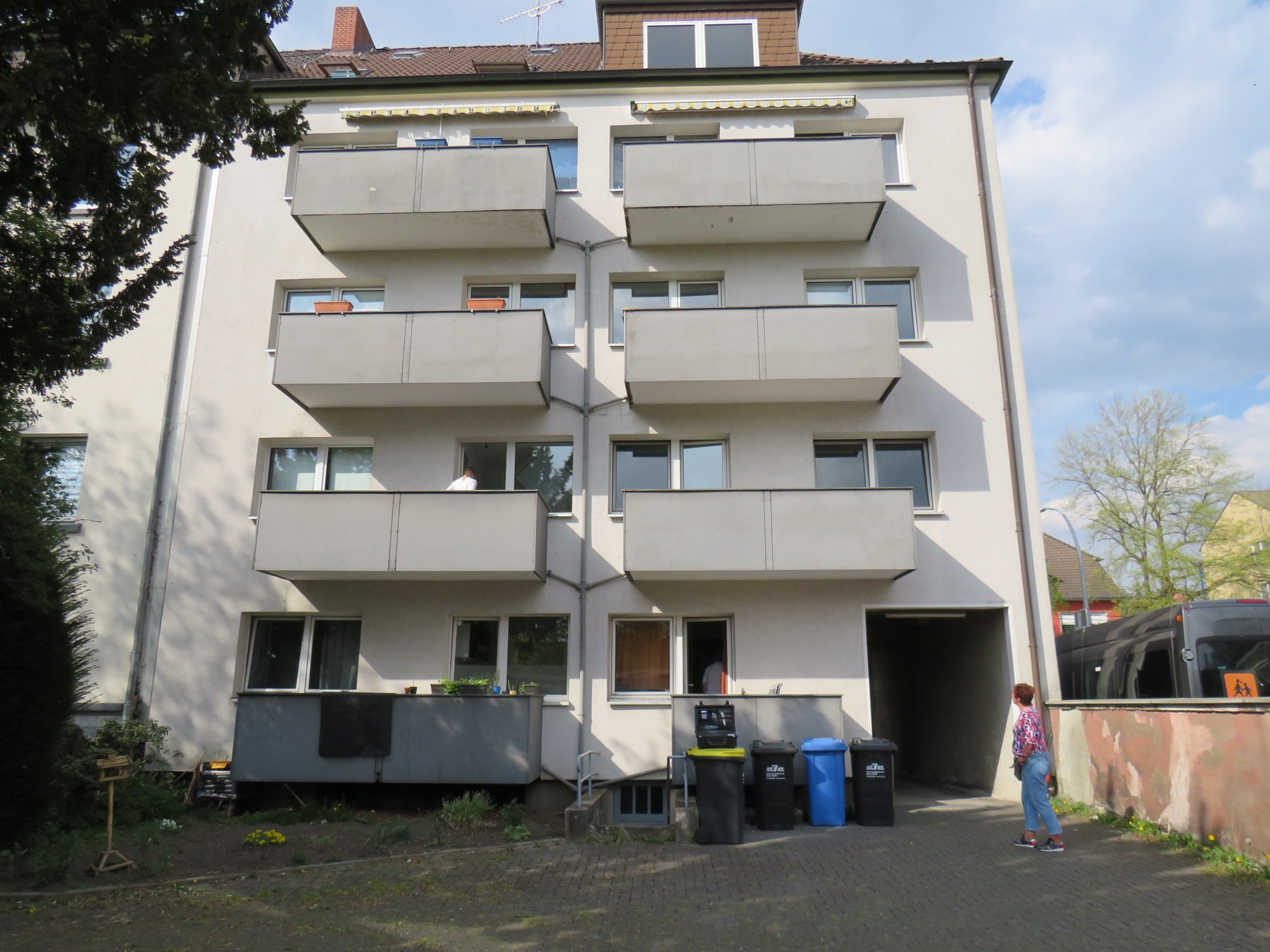 Mehrfamilienhaus mit Balkonen, Hofeinfahrt und Mülltonnen im Vordergrund