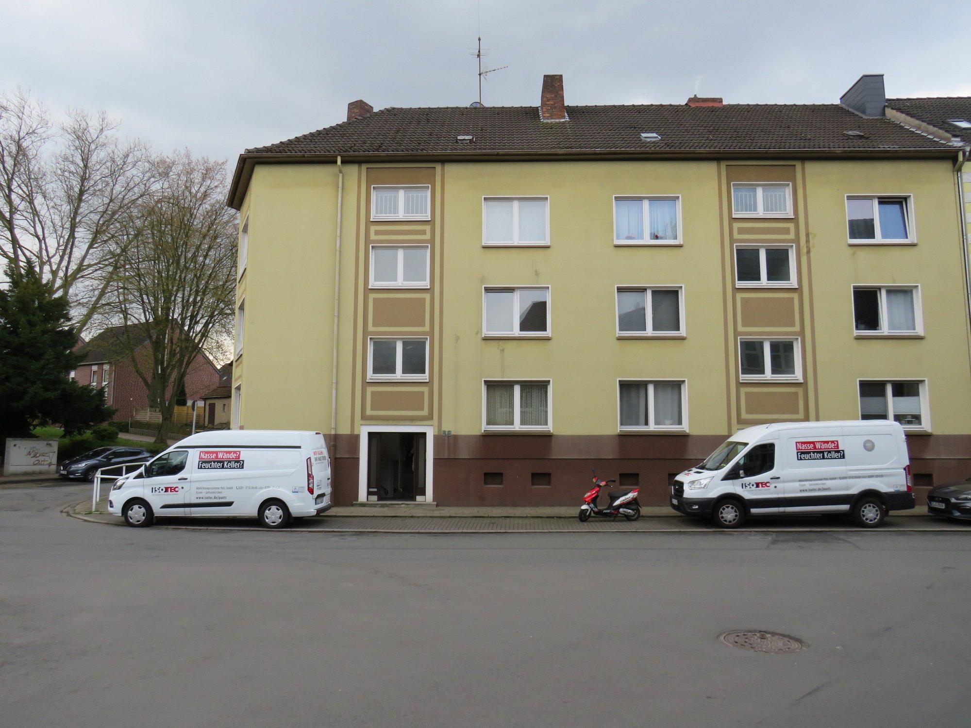 Mehrfamilienhausfassade mit zwei geparkten ISOTEC Transportern und Motorroller an der Straße