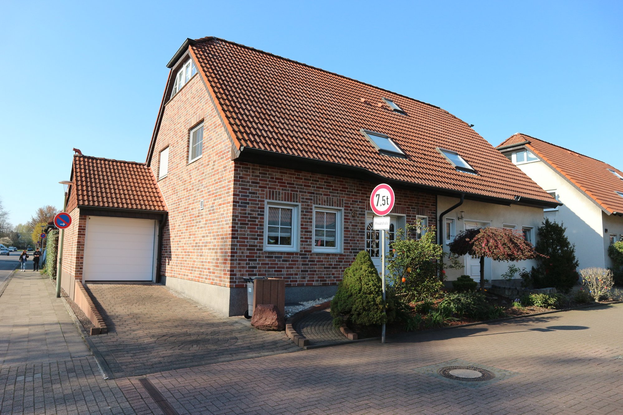 Einfamilienhaus aus Klinker mit rotem Ziegeldach, Garage und Vorgarten an Straße