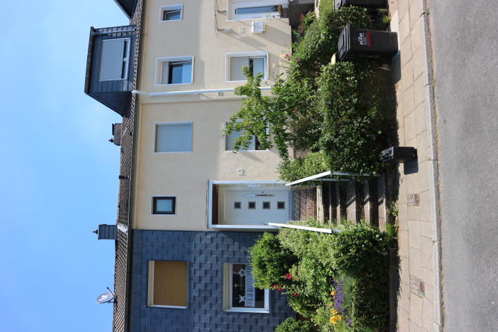 Straßenseite eines zweistöckigen Wohnhauses mit Eingangstreppe, Hecken und Blumenbeet.