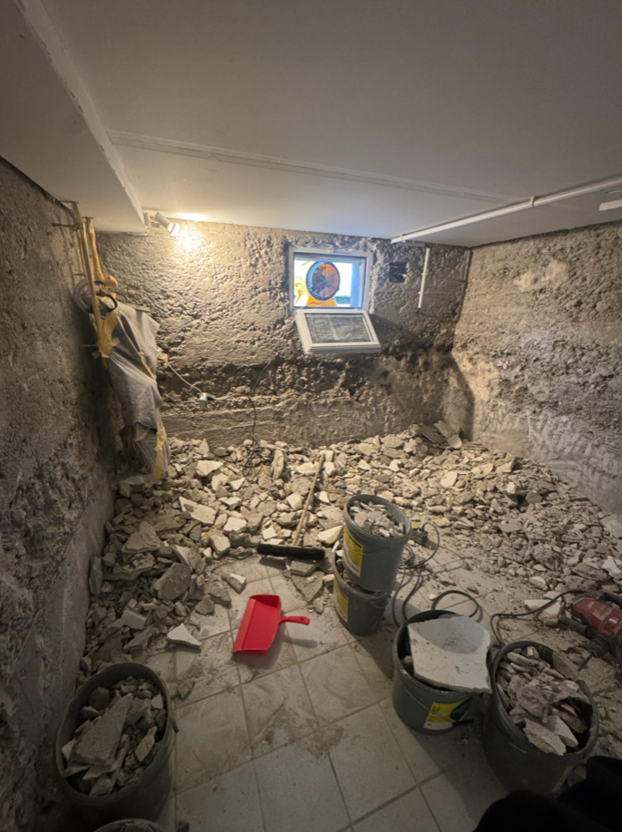 Schutt und aufgestemmte Wand in Kellerraum mit Eimern und Werkzeug