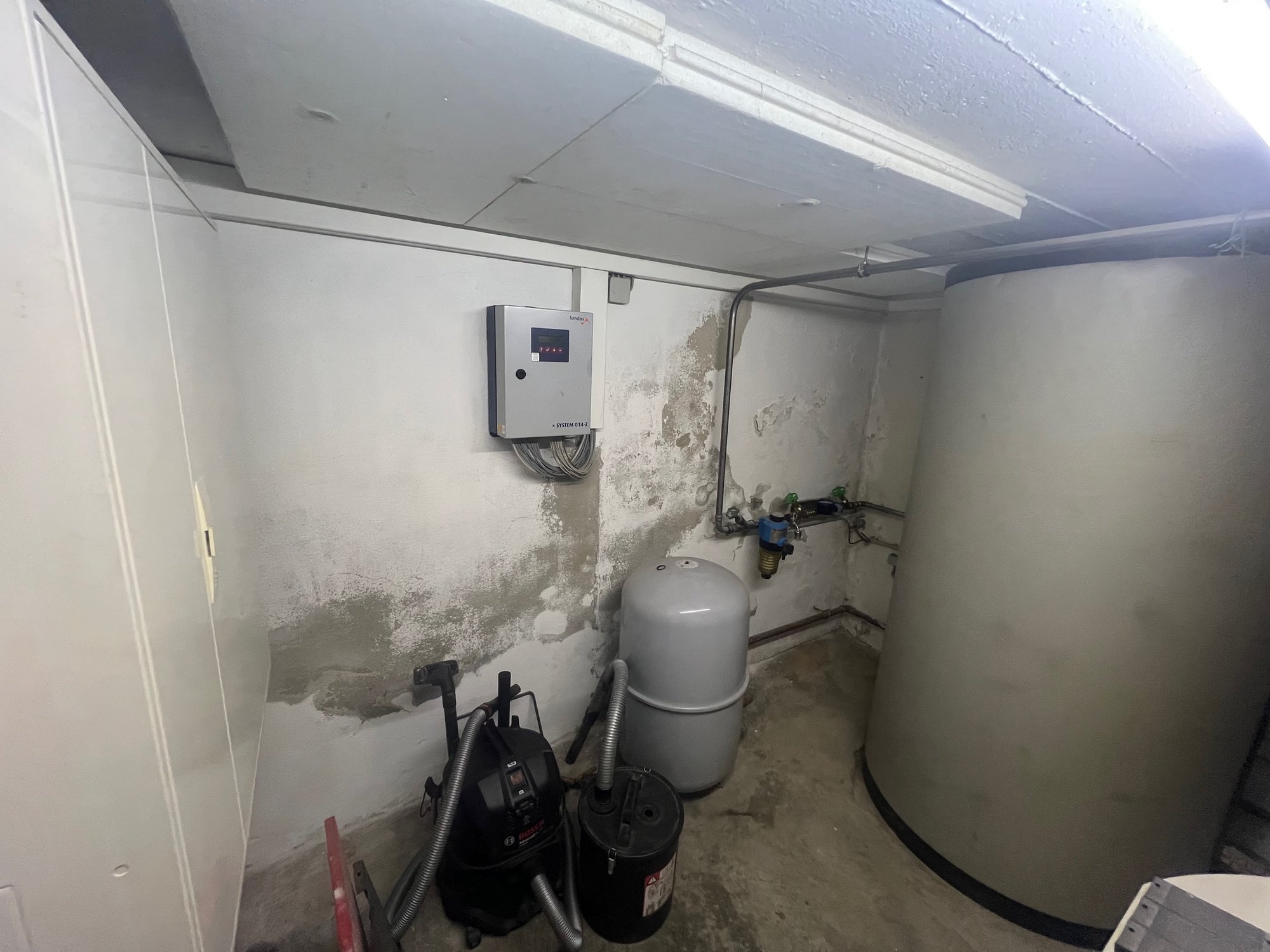 Feuchte Kellerwand mit Abplatzungen neben Technikbehältern