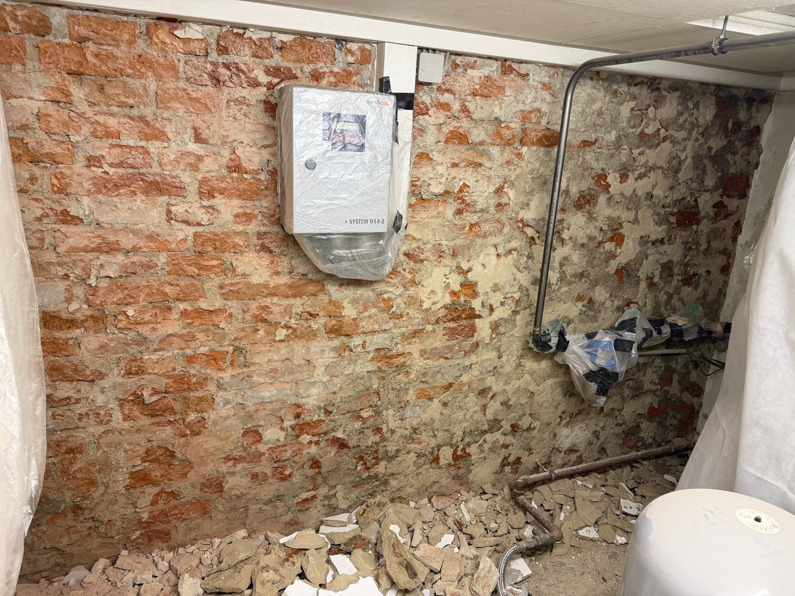 Freigelegte Ziegelwand mit Schutt und abgedeckten Leitungen