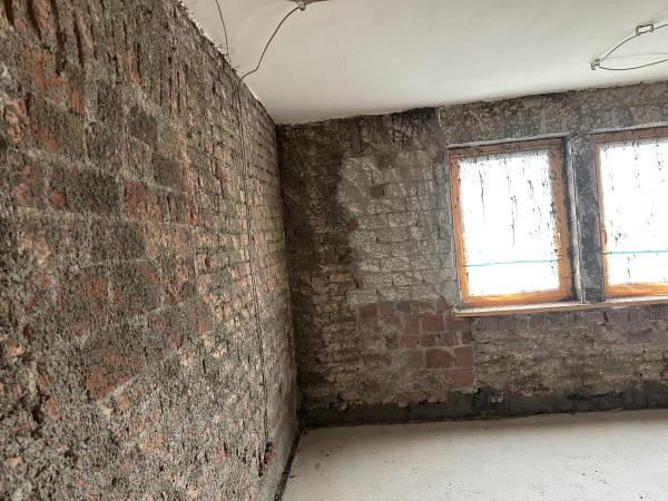 Freigelegte Kellerwand aus Ziegeln und grauer Masse mit feuchten Verfärbungen, Fenster rechts