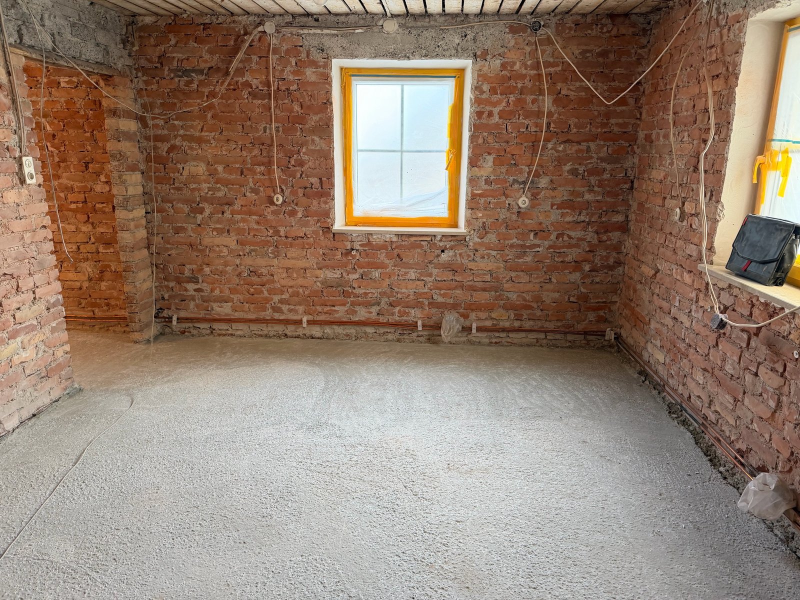 Entkernter Raum mit freigelegten Ziegelwänden, Fenstern und verlegten Elektrokabeln