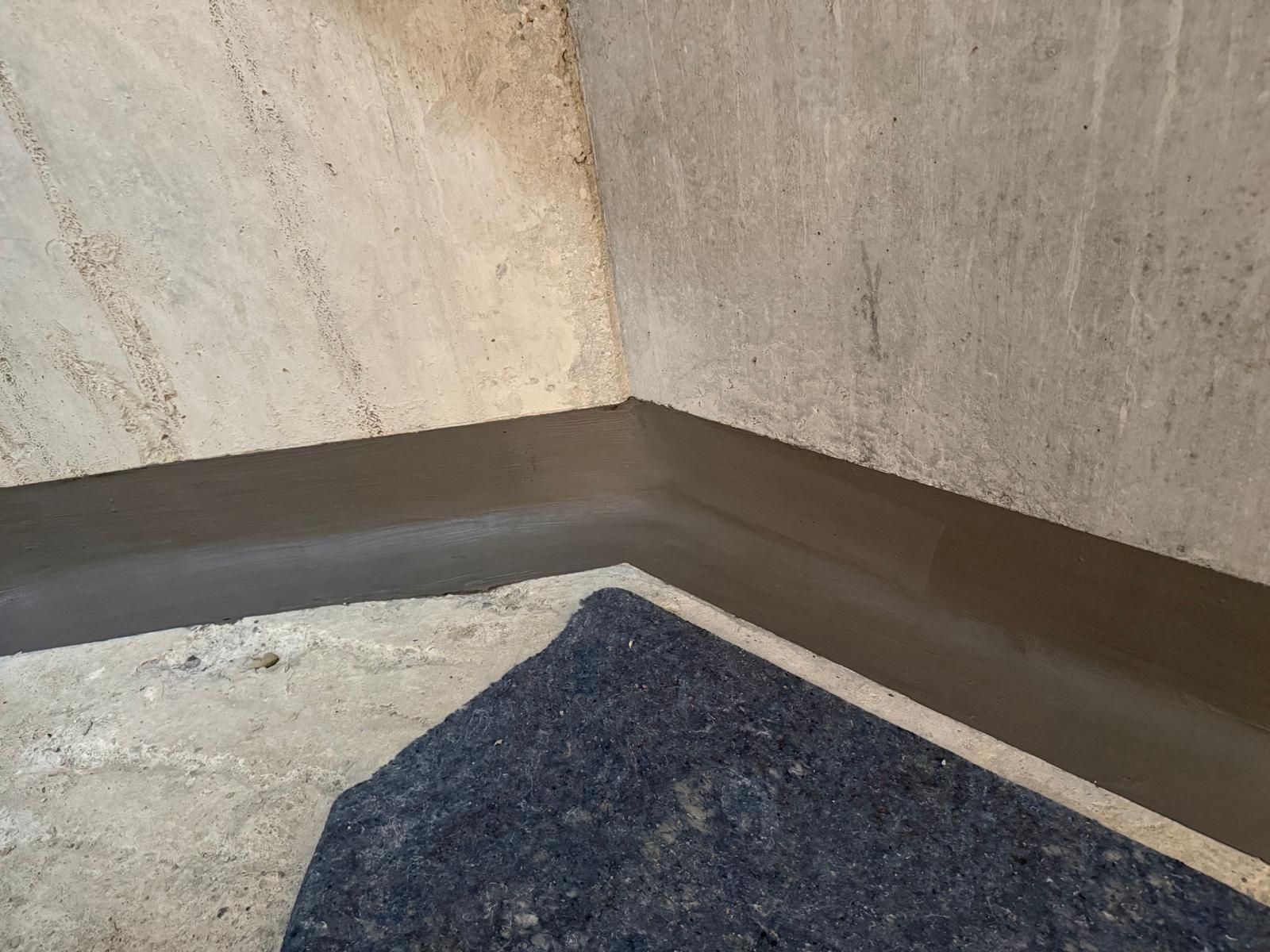 Schwarze Masse als Sockelbeschichtung in Betonecke, Boden mit dunkler Matte