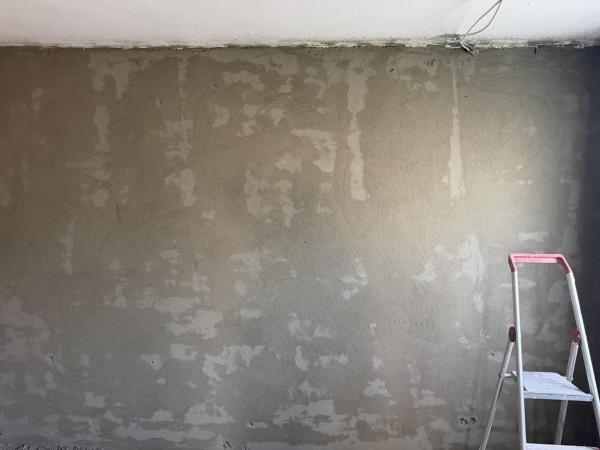 Graue Wand mit hellen Spachtelstellen, rechts eine Trittleiter im Zimmer.