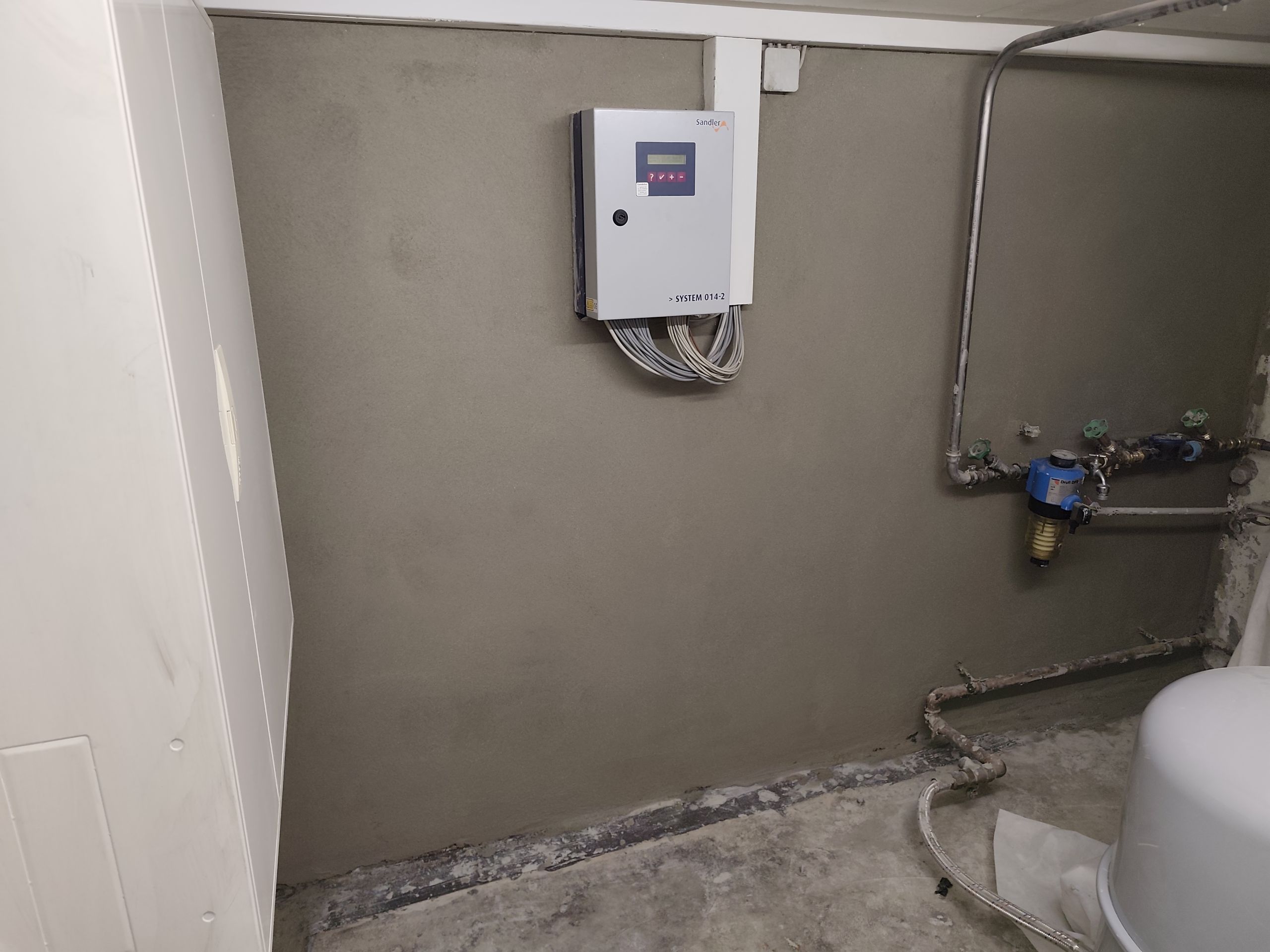 Technikraum mit grauer Wand, Steuergerät und Rohrleitungen.