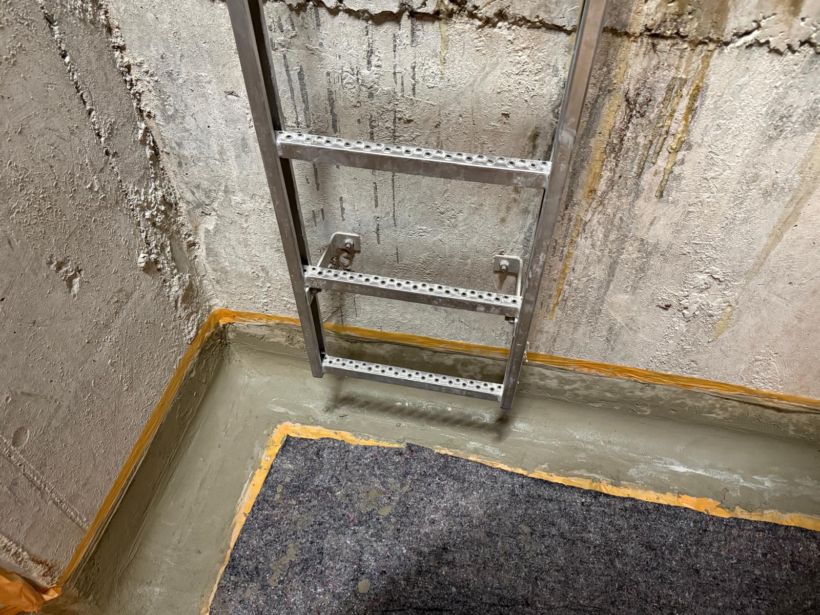 Aluminiumleiter vor rauer Kellerwand, graue Masse am Bodenrand mit orangefarbenem Klebeband