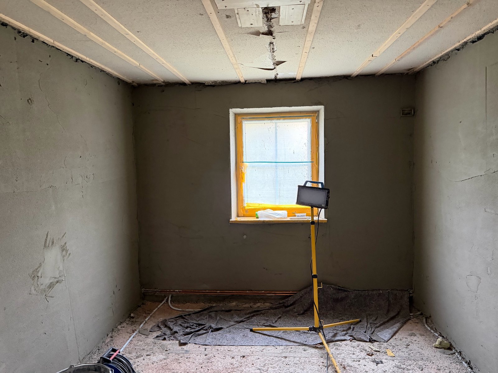 Sanierter Raum mit grauen Wänden, abgehängter Decke und Baustrahler vor Fenster