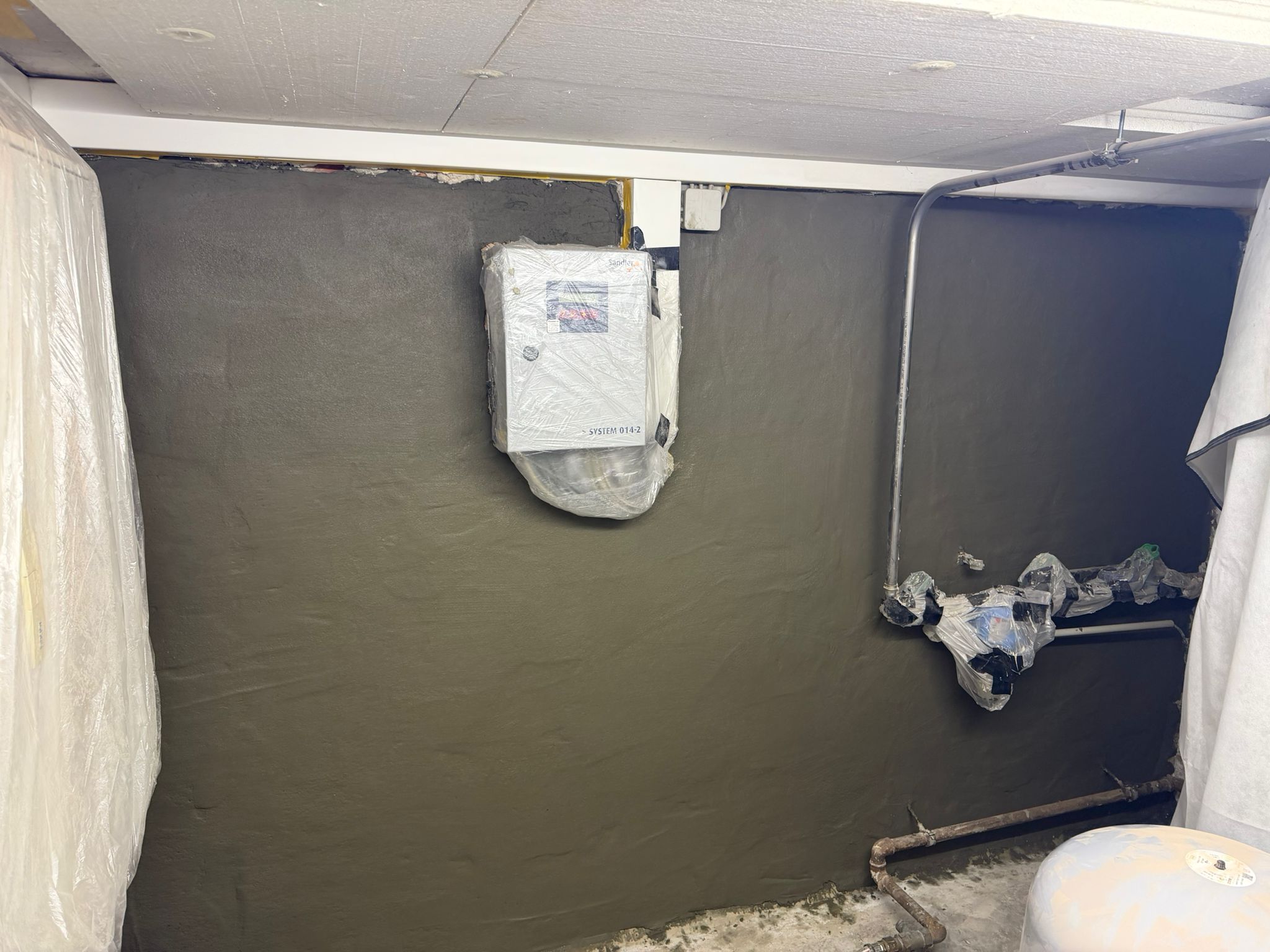 Mit grauer Masse beschichtete Kellerwand mit abgedeckten Leitungen