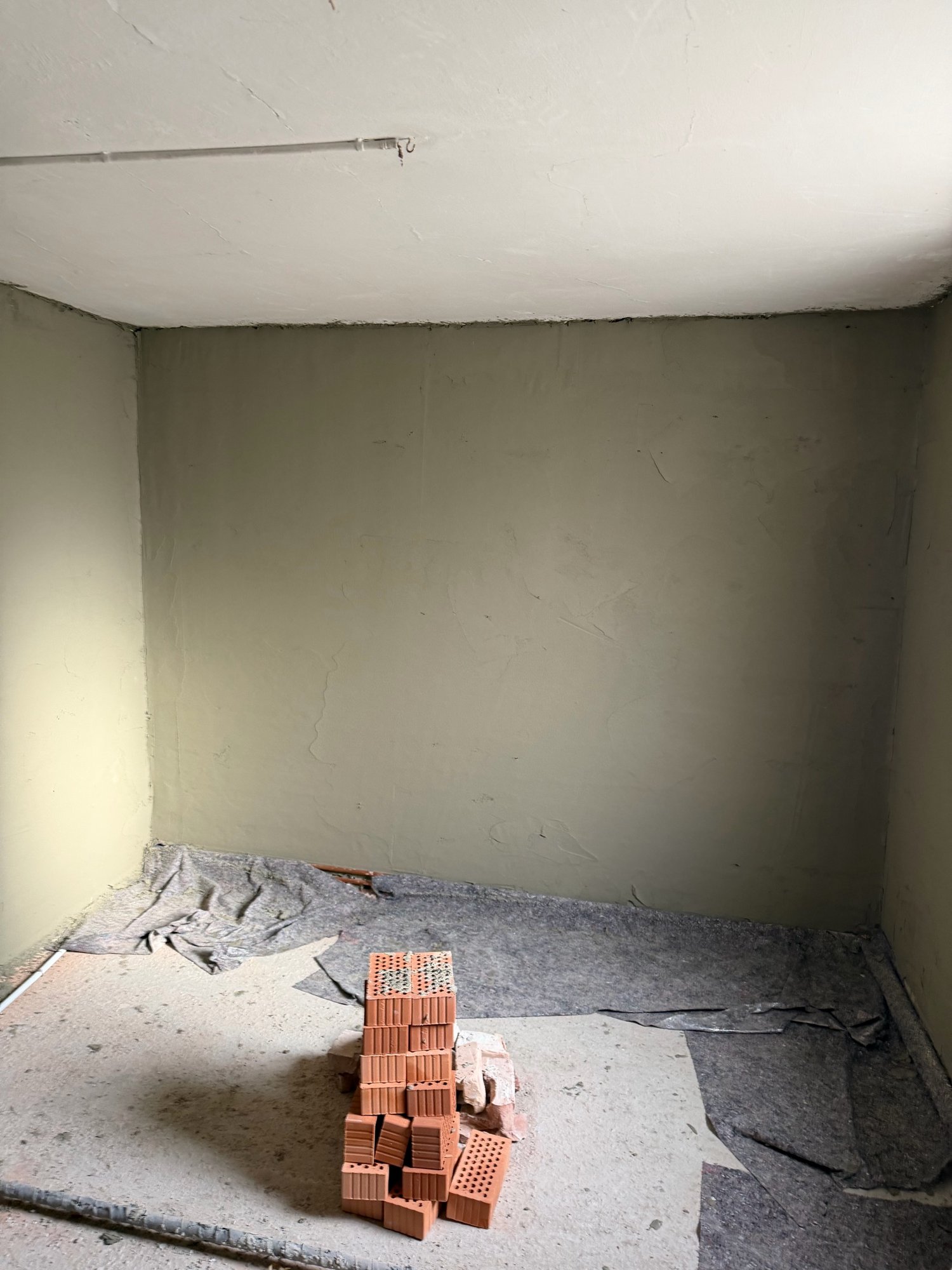Leerer Raum mit grauer Wandbeschichtung, blankem Boden und gestapelten Ziegelsteinen
