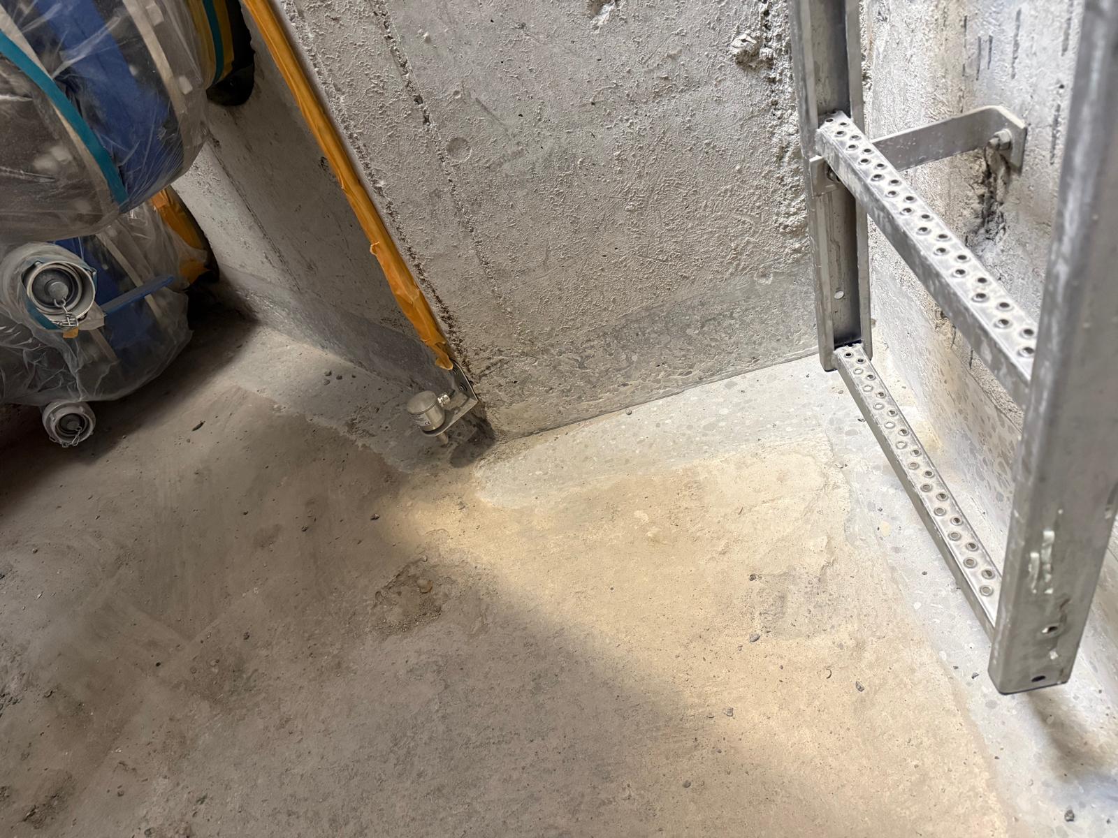 Betonecke mit grauer Wandfläche, Rohrleitung und Metallrahmen auf Betonboden