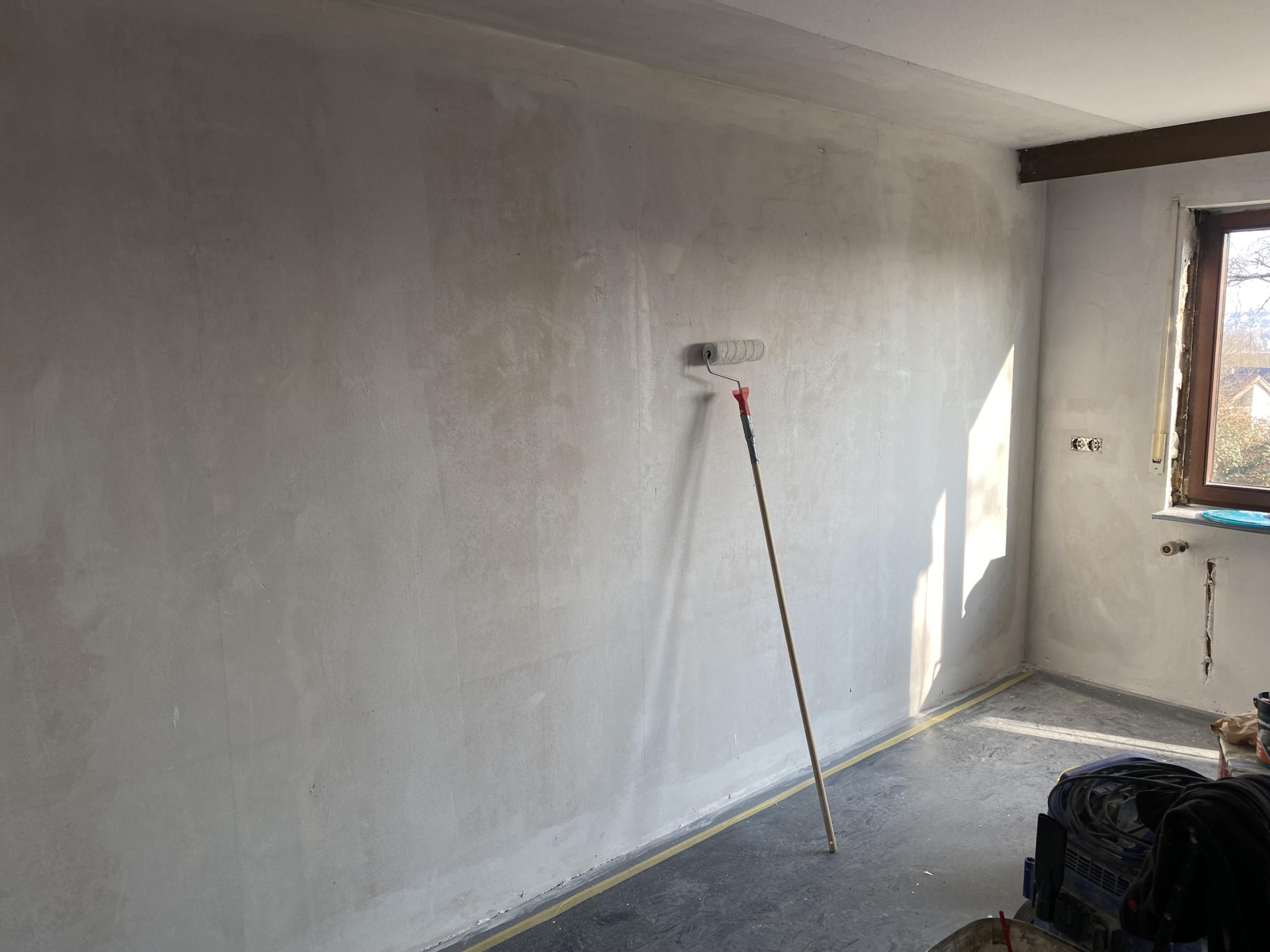 Farbroller lehnt an frisch beschichteter Zimmerwand im renovierten Raum
