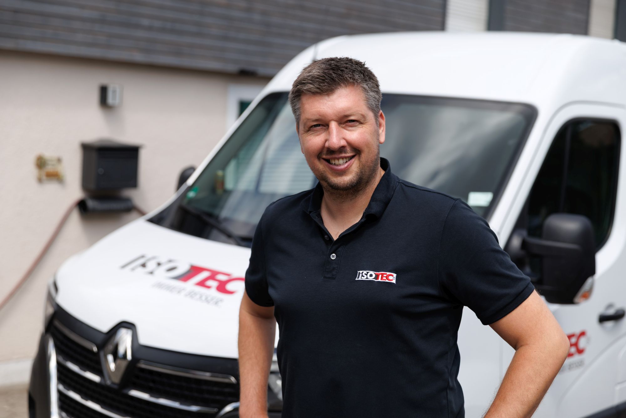 ISOTEC Mitarbeiter steht vor weißem Firmen-Transporter und lächelt in die Kamera.
