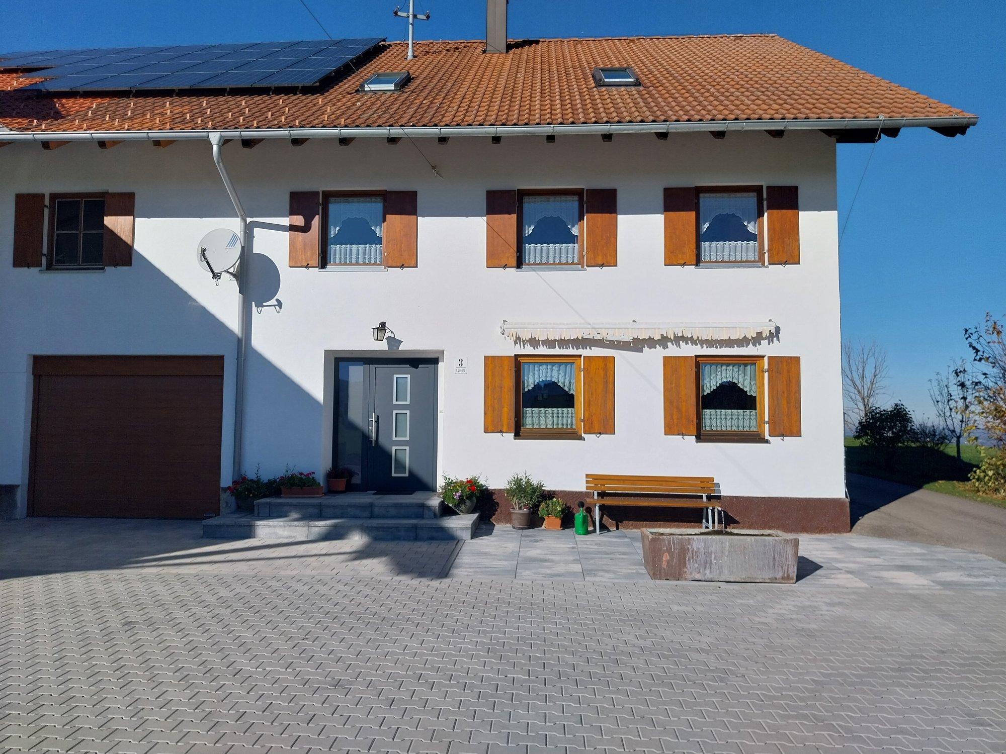 Weißes Wohnhaus mit Solarmodulen, Holzfenstern und gepflastertem Hof