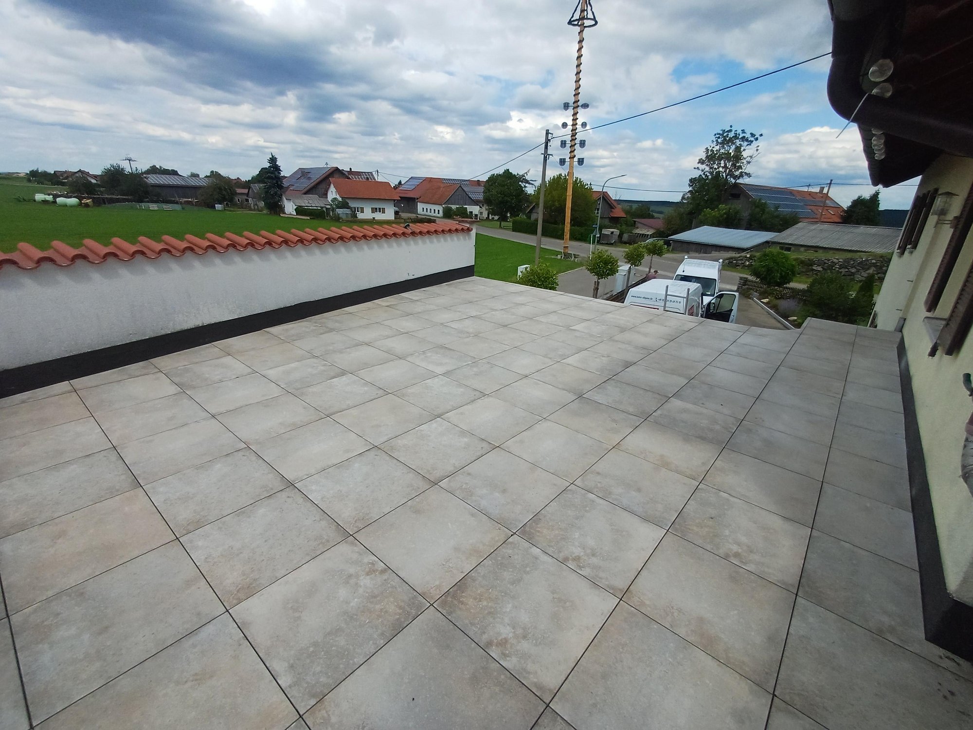 Geflieste Dachterrasse mit weißer Brüstung, Blick auf Dorfhäuser und Straße