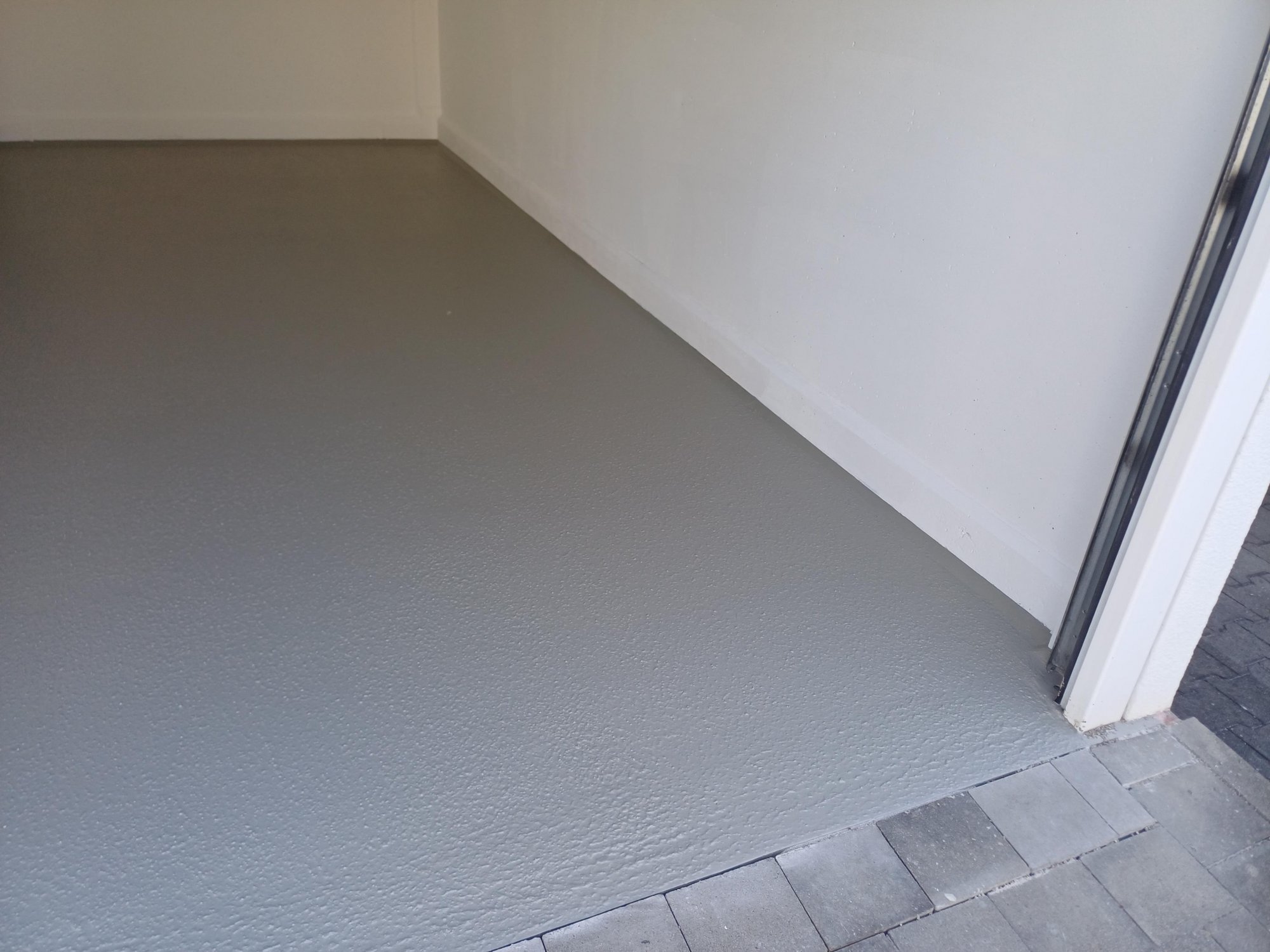 Grauer, strukturierter Bodenbelag am Eingang vor weißer Wand